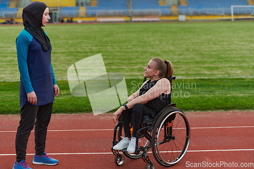 Image of A Muslim woman wearing a burqa resting with a woman with disability after a hard training session on the marathon course