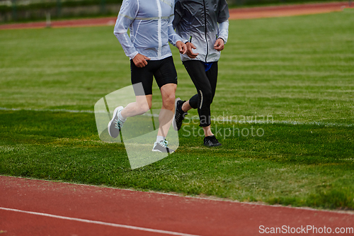 Image of An inspiring and active elderly couple showcase their dedication to fitness as they running together on a lush green field, captured in a close-up shot of their legs in motion.