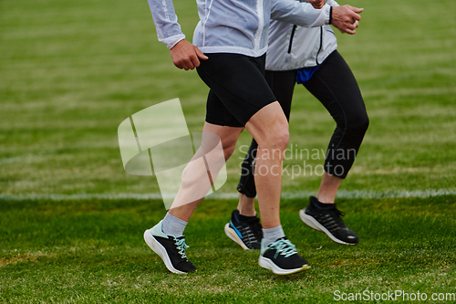 Image of An inspiring and active elderly couple showcase their dedication to fitness as they running together on a lush green field, captured in a close-up shot of their legs in motion.