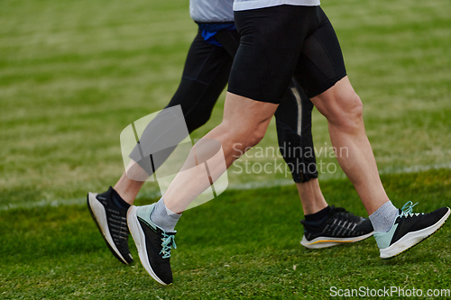 Image of An inspiring and active elderly couple showcase their dedication to fitness as they running together on a lush green field, captured in a close-up shot of their legs in motion.