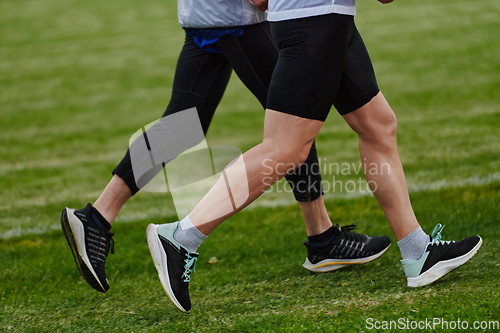 Image of An inspiring and active elderly couple showcase their dedication to fitness as they running together on a lush green field, captured in a close-up shot of their legs in motion.