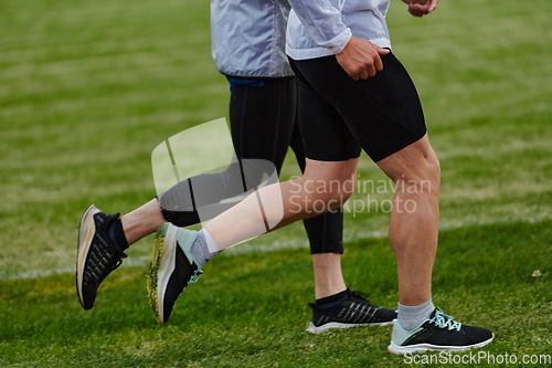 Image of An inspiring and active elderly couple showcase their dedication to fitness as they running together on a lush green field, captured in a close-up shot of their legs in motion.