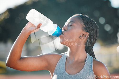 Image of Drinking water, sports and exercise with a woman outdoor for a run, training or workout. Thirsty African athlete person at stadium for fitness and body wellness with a bottle for hydration and break
