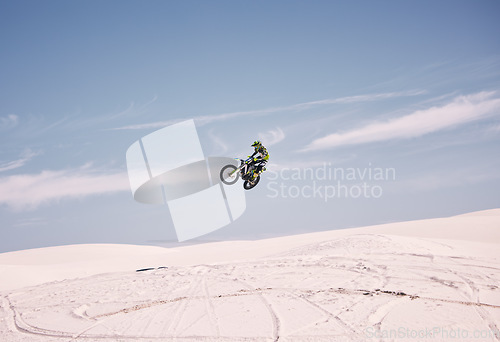 Image of Bike, sky and jump with a man in the desert riding a vehicle for adventure or adrenaline. Motorcycle, speed and training on sand with an athlete outdoor in nature for freedom or extreme sports