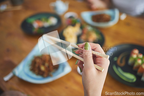 Image of Chopsticks, hand and a person eating food at a restaurant for nutrition. Closeup of a hungry woman with wooden sticks or utensil for dining, Japanese culture and cuisine on diet with sushi on menu