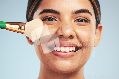 Image of Portrait, woman and smile with makeup brush in studio, apply foundation and glow on blue background. Face of happy young model with aesthetic cosmetics, skincare tools and beauty powder for self care