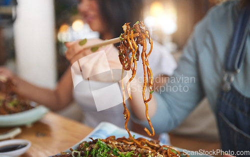 Image of Food, woman and hand with chopsticks in restaurant eat spaghetti and snack alone at table in closeup bokeh. Supper, person and meal, noodles on plate for lunch or asian dinner for nutrition