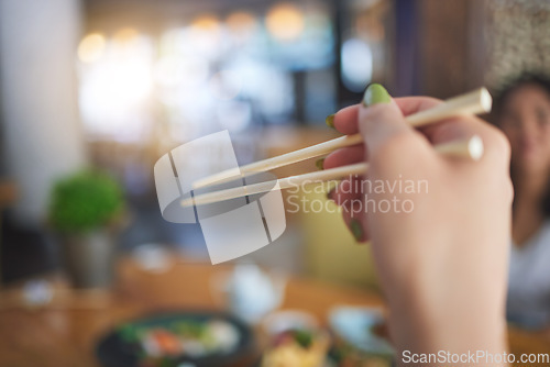 Image of Tradition, bamboo chopsticks and hand of a person eating Japanese food at a restaurant for nutrition. Closeup of a woman with wooden sticks or utensil for dining, culture and cuisine for diet