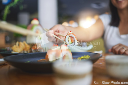 Image of Chopstick, hand and eating sushi food at restaurant for nutrition at table. Closeup of hungry people with wooden sticks for dining, Japanese culture and cuisine while sharing with creativity on plate