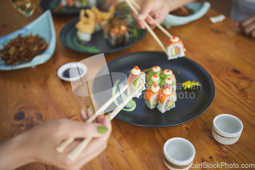 Image of Sushi, hands and eating food with chopsticks at restaurant for nutrition at table. Closeup of people with wooden sticks for dining, Japanese culture and cuisine while sharing with creativity on plate