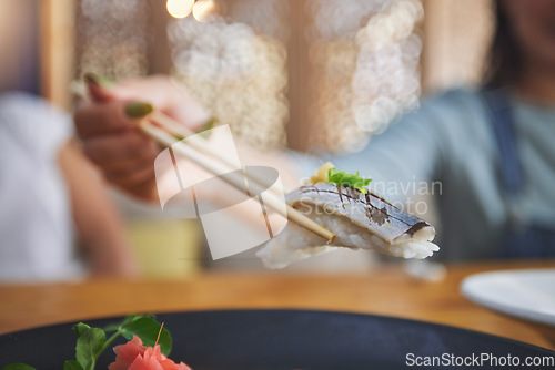 Image of Food, hand and eating sushi with chopsticks at restaurant for nutrition and health. Closeup of a hungry person with wooden sticks for dining, Japanese culture and cuisine with creativity on fish