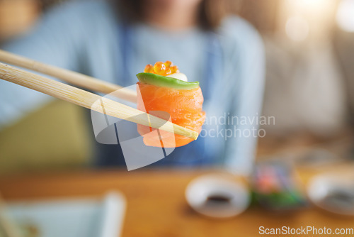 Image of Sushi, eating food and hand with chopsticks at restaurant for nutrition and health. Closeup of a person with wooden sticks for dining, Japanese culture and salmon cuisine with creativity on fish
