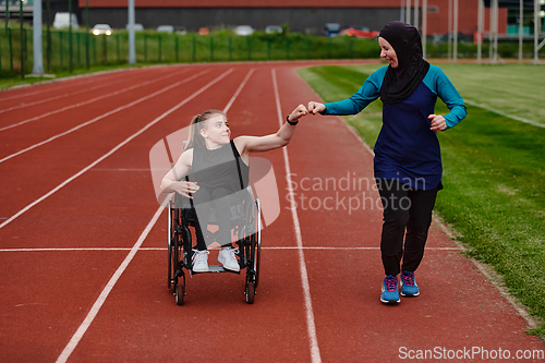 Image of A Muslim woman wearing a burqa supports her friend with disability in a wheelchair as they train together on a marathon course.