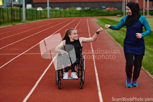 Image of A Muslim woman wearing a burqa supports her friend with disability in a wheelchair as they train together on a marathon course.