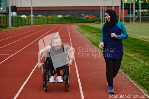 Image of A Muslim woman in a burqa running together with a woman in a wheelchair on the marathon course, preparing for future competitions.