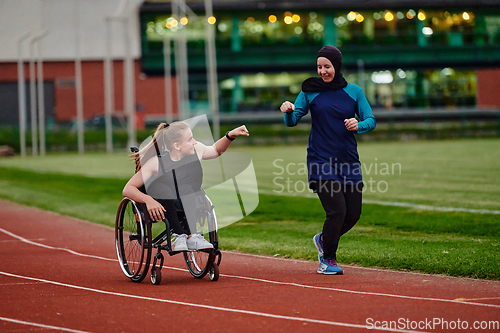 Image of A Muslim woman wearing a burqa supports her friend with disability in a wheelchair as they train together on a marathon course.