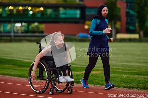 Image of A Muslim woman wearing a burqa supports her friend with disability in a wheelchair as they train together on a marathon course.