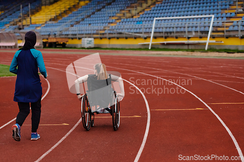 Image of A Muslim woman in a burqa running together with a woman in a wheelchair on the marathon course, preparing for future competitions.