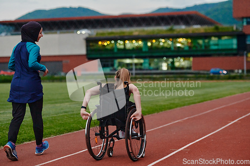 Image of A Muslim woman in a burqa running together with a woman in a wheelchair on the marathon course, preparing for future competitions.