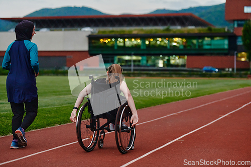 Image of A Muslim woman in a burqa running together with a woman in a wheelchair on the marathon course, preparing for future competitions.