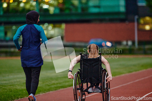 Image of A Muslim woman in a burqa running together with a woman in a wheelchair on the marathon course, preparing for future competitions.