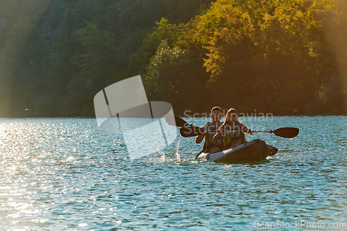 Image of A young couple enjoying an idyllic kayak ride in the middle of a beautiful river surrounded by forest greenery in sunset time