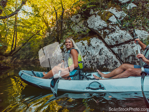 Image of A young couple enjoying an idyllic kayak ride in the middle of a beautiful river surrounded by forest greenery