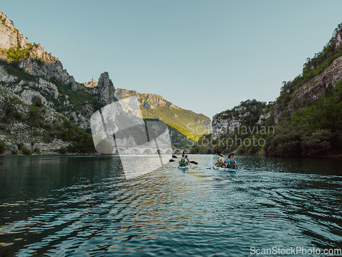 Image of A group of friends enjoying having fun and kayaking while exploring the calm river, surrounding forest and large natural river canyons