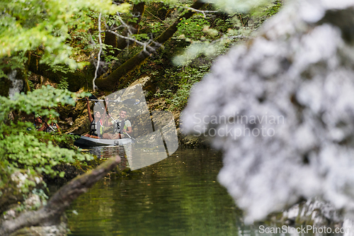 Image of A young couple enjoying an idyllic kayak ride in the middle of a beautiful river surrounded by forest greenery