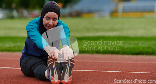 Image of A Muslim woman in a burqa, an Islamic sports outfit, is doing body exercises, stretching her neck, legs and back after a hard training session on the marathon course.