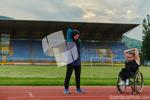 Image of Two strong and inspiring women, one a Muslim wearing a burka and the other in a wheelchair stretching and preparing their bodies for a marathon race on the track