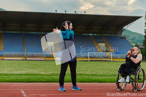 Image of Two strong and inspiring women, one a Muslim wearing a burka and the other in a wheelchair stretching and preparing their bodies for a marathon race on the track