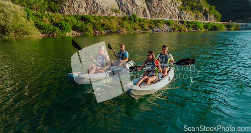 Image of A group of friends enjoying fun and kayaking exploring the calm river, surrounding forest and large natural river canyons during an idyllic sunset.