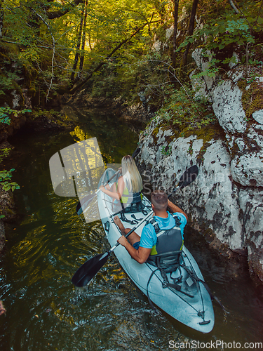 Image of A young couple enjoying an idyllic kayak ride in the middle of a beautiful river surrounded by forest greenery