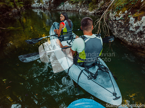 Image of A young couple enjoying an idyllic kayak ride in the middle of a beautiful river surrounded by forest greenery