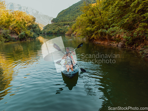 Image of A group of friends enjoying fun and kayaking exploring the calm river, surrounding forest and large natural river canyons during an idyllic sunset.