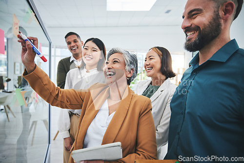 Image of Senior woman, writing and laughing at glass board for creative sticky notes with group agenda. Calendar planning, content creator schedule and management staff in a business meeting with teamwork