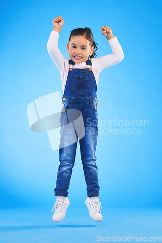 Image of Jump, smile and portrait of a child in a studio with energy, achievement or good news with excitement. Happy, youth and full length of a girl kid model moving for winning by isolated blue background.