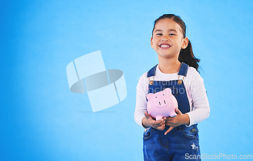 Image of Girl child, piggy bank and studio portrait with mockup space, saving and financial education by blue background. Female kid, money box and happy with goal, investing and learning discipline with cash