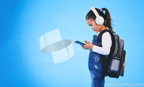 Image of Music, backpack and child on blue background with phone ready for school, learning and education. Kindergarten, studio and young girl with bag on smartphone for streaming song, audio and radio