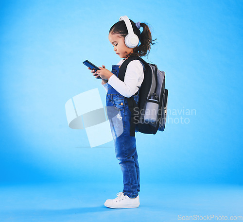 Image of Headphones, backpack and child on blue background with phone ready for school, learning and education. Kindergarten, and young girl with bag on smartphone for streaming music, audio and radio