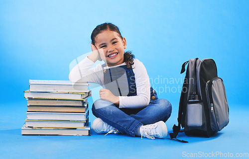 Image of Girl child, sitting and books in studio portrait, backpack and excited for learning on floor by blue background. Female kid, education and development with smile, future and studying for knowledge