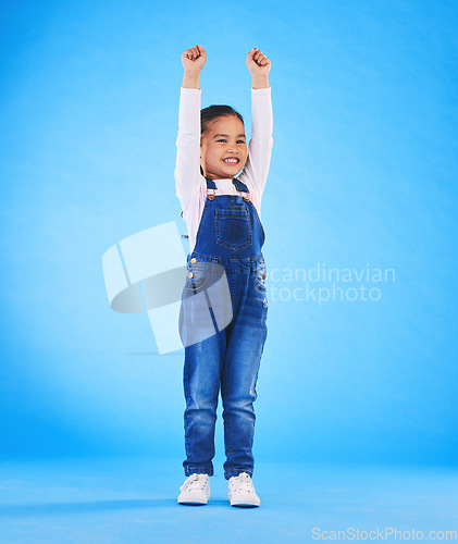 Image of Celebration, girl child and champion, winner and achievement with happiness and excited isolated on blue background. Cheers, yes and winning with success, pride and happy kid with arms up in a studio