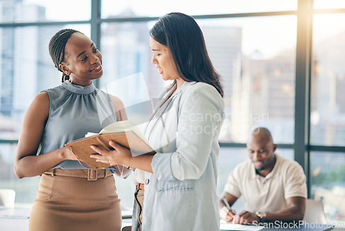 Image of Collaboration, diversity and notebook with business woman planning their schedule or calendar in the office. Teamwork, agenda and a professional employee reading a journal or diary with her colleague