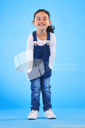 Image of Excited girl child, fashion and studio portrait with jeans, dungaree and trendy style by blue background. Female kid model, smile and happy for clothes, aesthetic and youth culture by backdrop