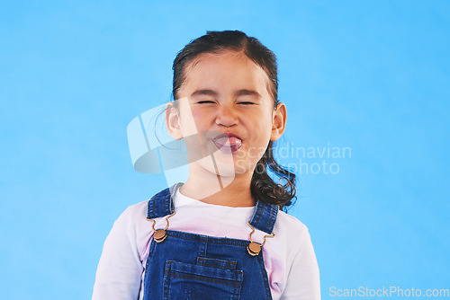 Image of Funny, face of child and girl with silly, goofy or facial expression on blue background in studio with fashion for children. Kid, portrait and tongue out of mouth in joke, humor or emoji for comedy