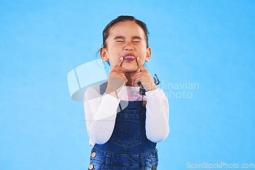 Image of Child, funny, face and girl with silly, goofy or facial expression on blue background in studio with fashion for children. Kid, portrait and tongue out of mouth in joke, humor or emoji for comedy