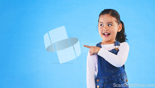 Image of Pointing, blue background and child with mockup space for banner, advertising and promotion. Excited, happy and young girl in studio with hand gesture for discount information, announcement and news