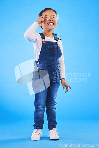 Image of Girl child, glasses and smile in studio with vision, health and thinking for eye care by blue background. Female kid, test spectacles and young fashion model with lens, frame and excited for wellness