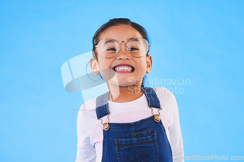 Image of Girl kid, glasses and vision in studio with smile, medical and thinking for eye care by blue background. Female child, test spectacles and young fashion model with lens, frame and excited for health